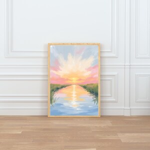 May include: A framed landscape painting depicts a sunset over a body of water. The artwork features a vibrant sky with pink, orange, and yellow hues, reflecting in the water. Green grass lines the water's edge.