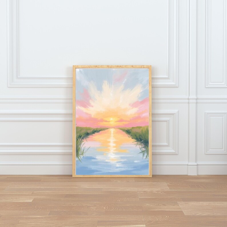 May include: A framed landscape painting depicts a sunset over a body of water. The artwork features a vibrant sky with pink, orange, and yellow hues, reflecting in the water. Green grass lines the water's edge.