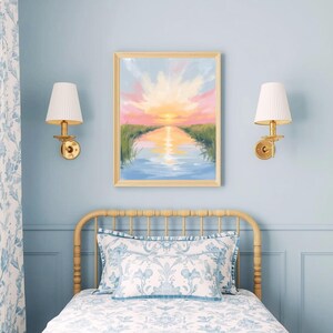 May include: A framed landscape painting depicts a sunset over a calm body of water, with pink, orange, and yellow hues in the sky. The artwork hangs above a bed with floral patterned bedding and a light-colored wooden headboard. Two wall sconces with white shades flank the painting.
