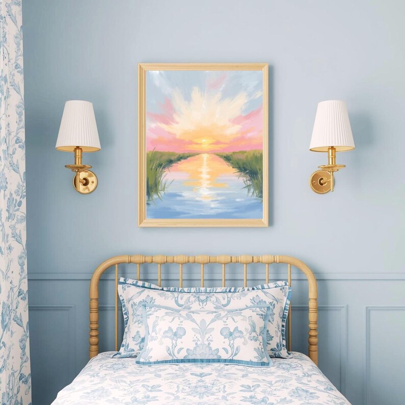 May include: A framed landscape painting depicts a sunset over a calm body of water, with pink, orange, and yellow hues in the sky. The artwork hangs above a bed with floral patterned bedding and a light-colored wooden headboard. Two wall sconces with white shades flank the painting.