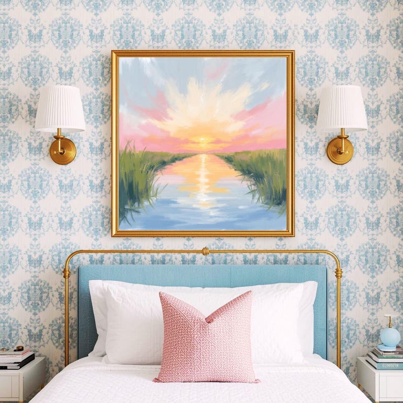 May include: A framed landscape painting depicts a sunset over a waterway, with pink, orange, and blue hues. The artwork is displayed above a bed with a blue headboard, white bedding, and a pink pillow. Gold sconces and a patterned wallpaper complete the bedroom decor.