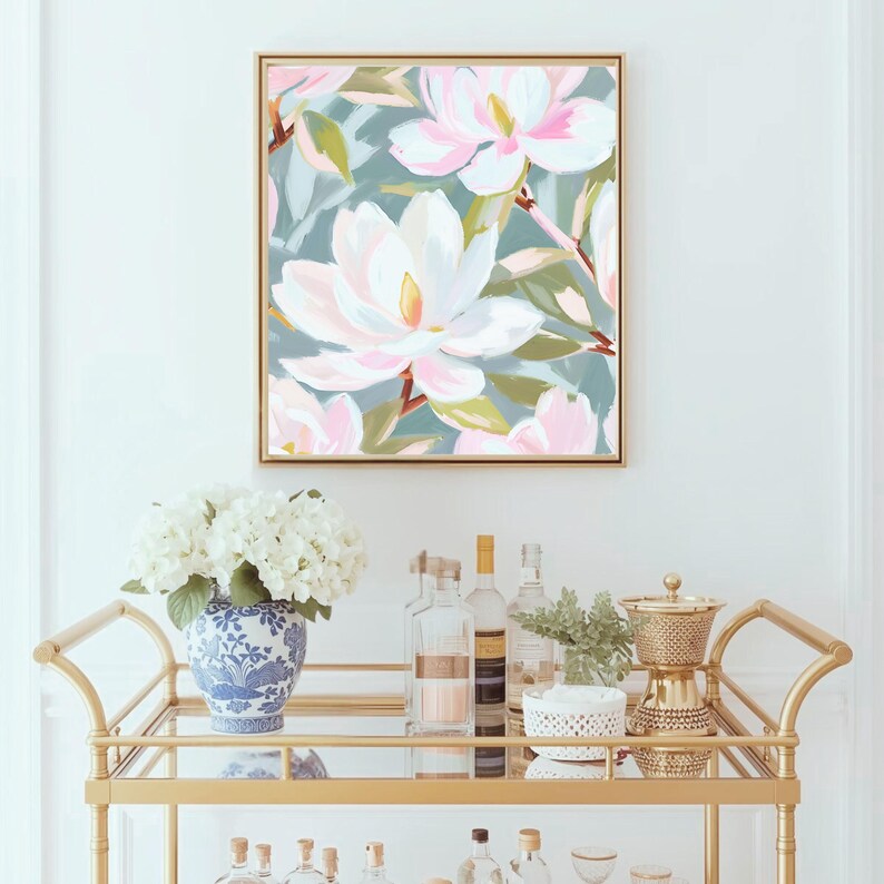 K&ouml;nnte beinhalten: Gerahmtes Blumenbild mit gro&szlig;en wei&szlig;en und rosa Magnolienbl&uuml;ten. Das Gem&auml;lde h&auml;ngt &uuml;ber einem goldenen Servierwagen mit einer blau-wei&szlig;en Vase mit wei&szlig;en Blumen, Flaschen und einer goldenen Kaffeemaschine.