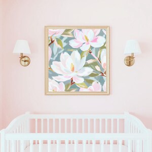 K&ouml;nnte beinhalten: Ein gerahmter Kunstdruck mit gro&szlig;en wei&szlig;en und rosa Magnolienbl&uuml;ten vor einem ged&auml;mpften tealfarbenen Hintergrund. Das Kunstwerk befindet sich in einem goldenen Rahmen und h&auml;ngt &uuml;ber einem wei&szlig;en Kinderbett in einem rosa Raum. Zwei goldene Wandleuchten mit wei&szlig;en Schirmen flankieren das Kunstwerk.