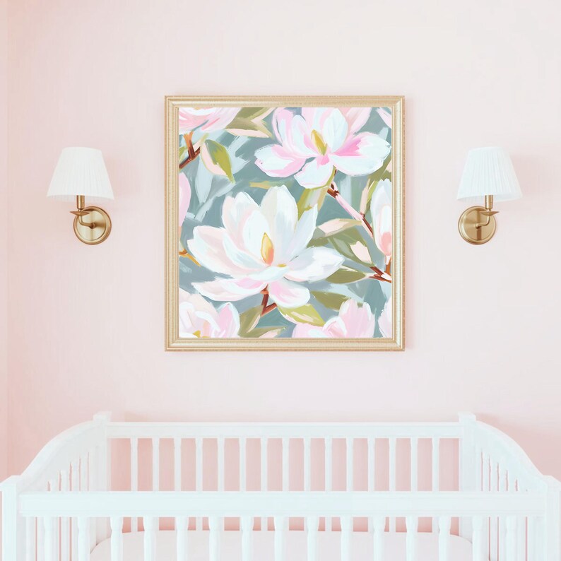 K&ouml;nnte beinhalten: Ein gerahmter Kunstdruck mit gro&szlig;en wei&szlig;en und rosa Magnolienbl&uuml;ten vor einem ged&auml;mpften tealfarbenen Hintergrund. Das Kunstwerk befindet sich in einem goldenen Rahmen und h&auml;ngt &uuml;ber einem wei&szlig;en Kinderbett in einem rosa Raum. Zwei goldene Wandleuchten mit wei&szlig;en Schirmen flankieren das Kunstwerk.