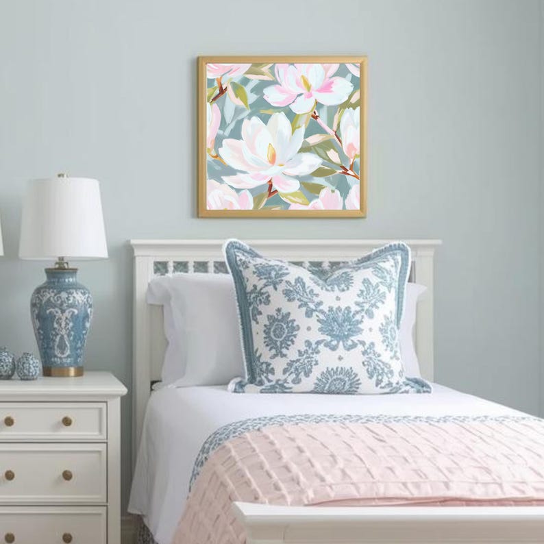K&ouml;nnte beinhalten: Ein Schlafzimmer mit einem gerahmten Blumendruck mit wei&szlig;en und rosa Magnolienbl&uuml;ten. Das Bett hat ein wei&szlig;es Kopfteil, ein blau gemustertes Kissen und eine rosa Decke. Eine blau-wei&szlig;e Lampe steht auf einem wei&szlig;en Nachttisch.