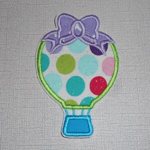 May include: A colorful hot air balloon with a purple bow on top. The balloon is decorated with polka dots in shades of blue, green, red, and pink.