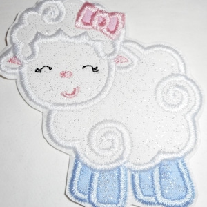 May include: A white, glittery sheep patch with a pink bow, ears, and nose. The sheep has blue legs and a smiling face. The patch is an embroidered applique, suitable for clothing or craft projects.