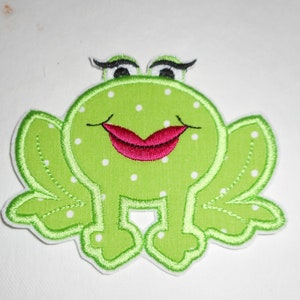 May include: Green frog applique with white polka dots and a red mouth. The frog has eyelashes and is embroidered.