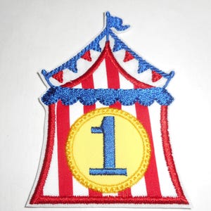 May include: An embroidered patch shaped like a circus tent with red and white vertical stripes. The tent features a blue scalloped trim, a blue flag at the peak, and a central yellow circular emblem containing a large, bold blue number one.