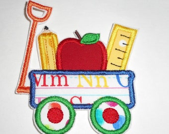 May include: A red, yellow, and green embroidered patch of a wagon filled with school supplies. The wagon has a blue base with the letters "Mm Nn Uu" on the side. The wagon has two green wheels with red centers.
