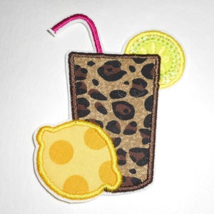 May include: A brown and black leopard print glass with a pink straw and two yellow lemons. The lemons have a yellow outline and white dots.