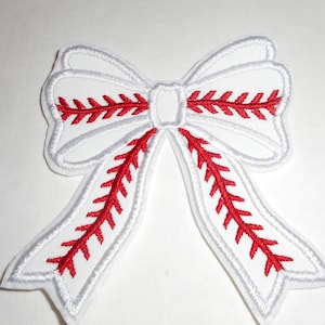May include: A white embroidered patch in the shape of a bow. The bow features red stitching that mimics the appearance of baseball laces, with a white border outlining the entire shape of the bow and its two long, flowing ribbon tails.