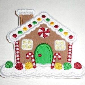 May include: A gingerbread house applique with white frosting, red and white candy canes, and green and yellow candy dots. The house has a green door and two windows with yellow panes.