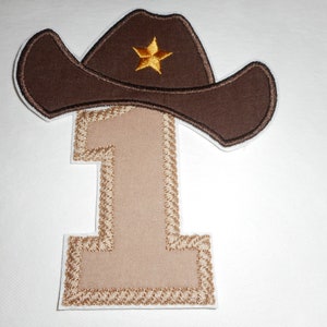 May include: Embroidered patch featuring a brown cowboy hat with a gold star and the number "1". The number is tan with a decorative border. The patch is designed for a first birthday or Western-themed event.