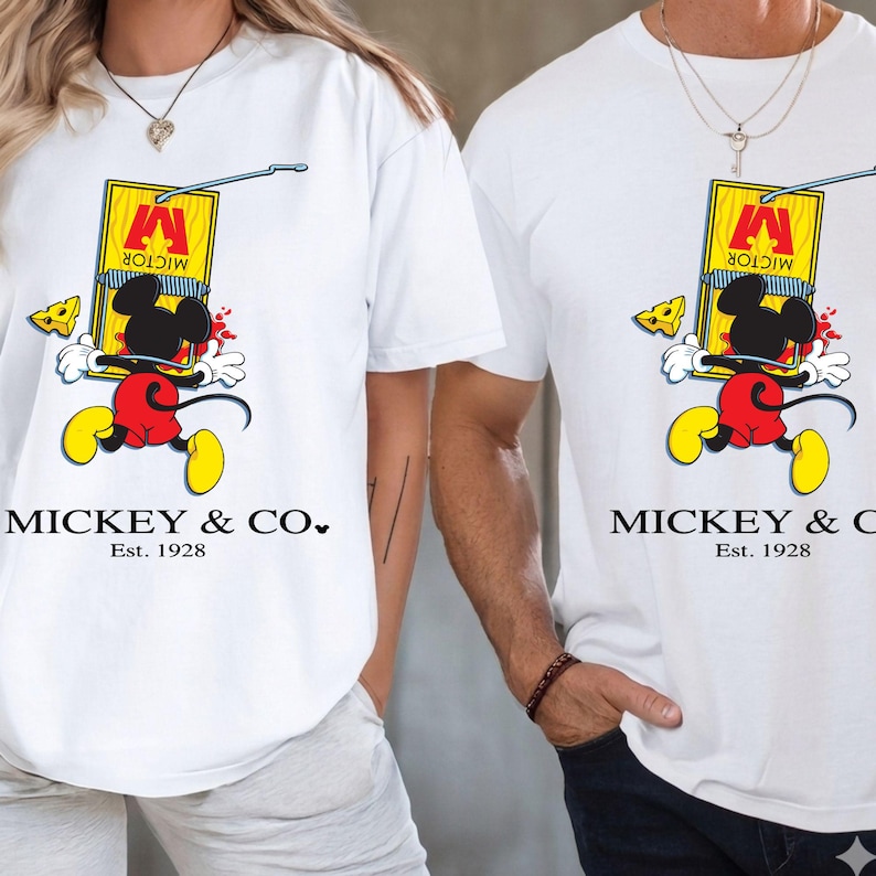Pu&ograve; includere: T-shirt bianche con un design a cartone animato di Mickey Mouse. La grafica mostra Mickey Mouse che corre con una trappola per topi, formaggio e il testo "MICKEY & CO." e "Est. 1928". Il design &egrave; in rosso, giallo, nero e bianco.