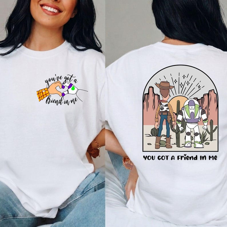 May include: A white t-shirt featuring a small chest graphic of a human hand and a robot hand forming a heart shape with the text you've got a friend in me. The back displays a desert scene with a cowboy and a space ranger with the text YOU GOT A FRIEND IN ME.