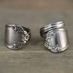 Op de afbeelding: Twee zilveren lepelringen met bloemendetails. De ringen zijn gemaakt van hergebruikt bestek, wat ze een vintage uitstraling geeft. De lepels vormen de ringvlakken, met het bloemendesign dat een vleugje elegantie toevoegt.