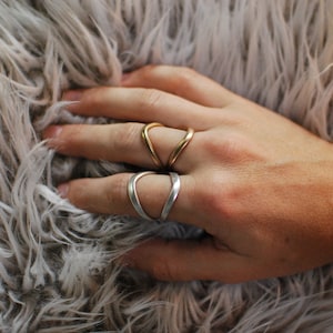 Op de afbeelding: Twee gouden en zilveren ringen aan een vinger. De ringen zijn beide open en hebben een gebogen vorm.