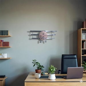 Op de afbeelding: Metalen wanddecoratie in de vorm van een vliegtuig. Het stuk heeft een cirkelvormige wijzerplaat met een koperen afwerking en zilverkleurige vleugels. Onder de wijzerplaat zitten twee haken om items op te hangen.