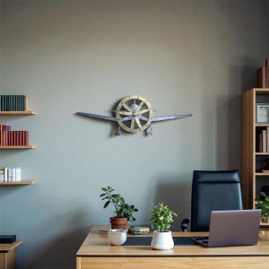 May include: A decorative wall clock in the shape of an aeroplane, featuring a propeller-style clock face and silver wings. The clock is mounted on a grey wall in an office. The clock face has black numerals and hands.