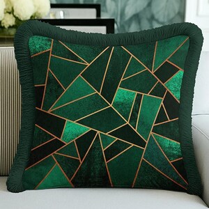 May include: A square throw pillow featuring a deep emerald green velvet-like texture with a geometric pattern of intersecting thin gold lines. The edges of the pillow are finished with a matching dark green gathered fabric fringe trim.