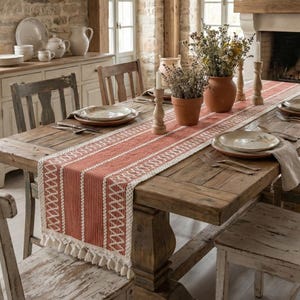 Può includere: Una sala da pranzo rustica con un grande tavolo in legno apparecchiato con piatti, tovaglioli e un runner da tavolo a motivi rossi e bianchi. Il tavolo è circondato da sedie in legno anticato. Vasi, candele, un camino e pareti in pietra completano l'atmosfera.
