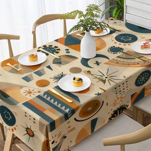 Könnte beinhalten: Eine rechteckige Tischdecke mit einem geometrischen Muster in Creme, Dunkelblau und Orange. Das Design zeigt abstrakte Formen, Sonnenstrahlen und Sternmotive. Eine weiße Vase und vier weiße Teller mit kleinen Desserts stehen auf dem Tisch.