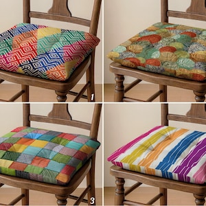 Könnte beinhalten: Vier quadratische Stuhlkissen mit verschiedenen bunten Mustern. Die Kissen sind auf Holzstühlen platziert. Die Muster umfassen geometrische Designs, florale Motive, Patchwork und Streifen. Die Kissen verleihen den Stühlen ein dekoratives Element.