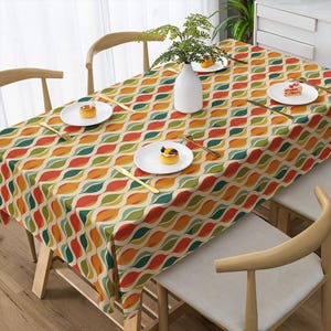 May include: A rectangular tablecloth featuring a repeating wavy pattern in shades of orange, red, olive green, and cream. The fabric covers a dining table set with four white plates, gold-toned cutlery, and a white vase containing greenery.