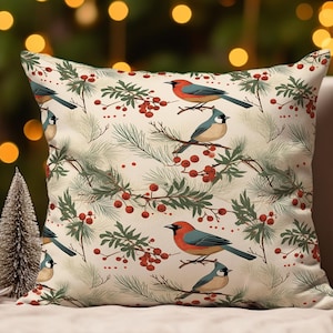 Può includere: Cuscino quadrato con sfondo color crema con un motivo ripetuto di uccelli, bacche rosse e rami di pino verdi. Gli uccelli hanno colori rosso, blu e beige. Il cuscino è su uno sfondo neutro con luci sfocate.