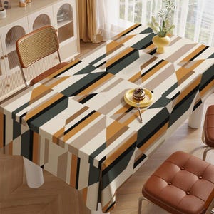 Puede incluir: Mantel rectangular con un patrón geométrico en tonos beige, marrón, negro y verde oliva. La mesa está puesta con un plato amarillo pequeño que contiene un postre. La mesa está sostenida por patas blancas.