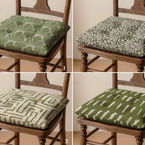 Könnte beinhalten: Vier quadratische Stuhlkissen mit verschiedenen Mustern. Die Kissen in Grün- und Weißtönen sind auf Holzstühlen platziert. Die Muster umfassen florale, geometrische und abstrakte Designs. Diese Kissen sind ein dekoratives Wohnaccessoire.