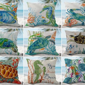 Könnte beinhalten: Set aus neun dekorativen Zierkissen mit Aquarelldesigns von Meereslebewesen. Kissen zeigen Bilder von Fisch, Seepferdchen, Krebs, Meeresschildkröte und Korallen. Die Kissen sind quadratisch und haben einen weißen Hintergrund mit einer Strandszene.