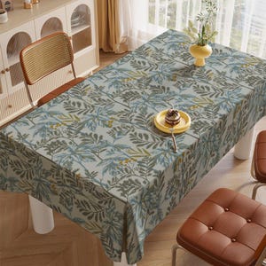 May include: A rectangular tablecloth with a botanical pattern in shades of gray, blue, and green. The tablecloth is draped over a table with white legs. A yellow plate with a dessert and a fork sits on the tablecloth.