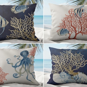 May include: Four square throw cushions with marine-themed designs. The cushions feature watercolour illustrations of fish, coral, and an octopus. The colour palette includes navy blue, white, and coral. The cushions appear to be made of a soft fabric.