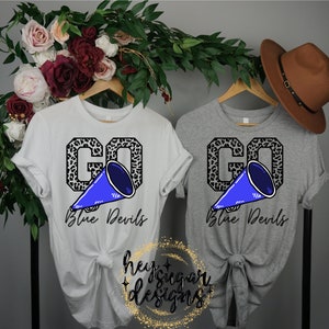 May include: Two t-shirts with a leopard print "GO" design and a blue megaphone. The text "Blue Devils" is below the design. One shirt is white and the other is gray.