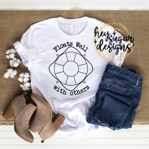 Puede incluir: Camiseta blanca con un gráfico de salvavidas negro y el texto "Floats Well with others".