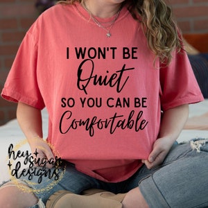 May include: A coral pink t-shirt with black text that reads "I won't be quiet so you can be comfortable."