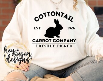May include: White sweatshirt with black text that reads "COTTONTAIL EST. 1926 CARROT COMPANY FRESHLY PICKED". A black silhouette of a rabbit is in the center of the text.