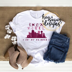 May include: White t-shirt with a burgundy graphic of the Knoxville skyline and the text "KNOXVILLE" and "35° 57' 52.8048".