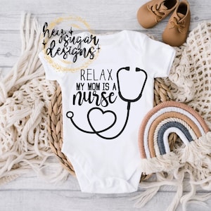 May include: White baby onesie with black text that reads "Relax my mom is a nurse" with a stethoscope and heart graphic.