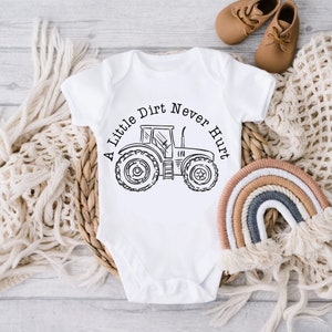 Puede incluir: Un body blanco para bebé con una ilustración en blanco y negro de un tractor y el texto "A Little Dirt Never Hurt".