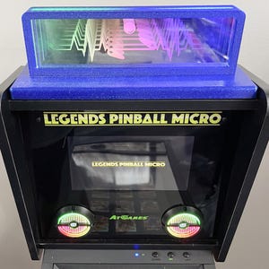May include: A black Legends Pinball Micro arcade machine with a blue glitter top and a clear display case. The machine has the text "LEGENDS PINBALL MICRO" in gold lettering. The screen displays "LEGENDS PINBALL MICRO".