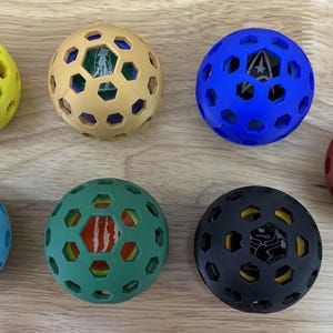 Peut inclure: Sept boules en plastique creuses et colorées avec des motifs différents à l'intérieur. Chaque boule a un motif hexagonal.
