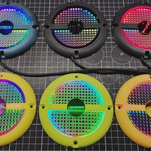 May include: Six circular LED light panels with different colour schemes. The panels have a perforated centre and a coloured border. Some panels have text that reads "TRON", "SPACE INVADERS", and "CENTIPEDE".