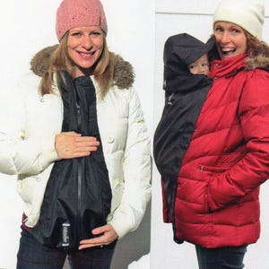 May include: Two women wearing winter jackets. One is white with a fur-trimmed hood, the other is red. Both jackets have a black insert for carrying a baby. The woman on the left is wearing a pink knit hat, and the woman on the right is wearing a white knit hat.