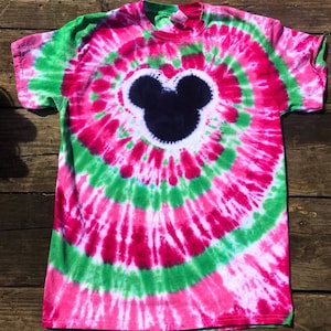 May include: A tie-dye t-shirt with a black Mickey Mouse silhouette in the center. The shirt is pink, green, and white.