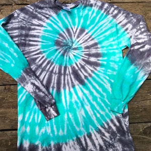 Może przedstawiać: Koszulka z długim rękawem z wzorem tie-dye w odcieniach turkusu, szarości i bieli. Koszulka ma spiralny wzór.