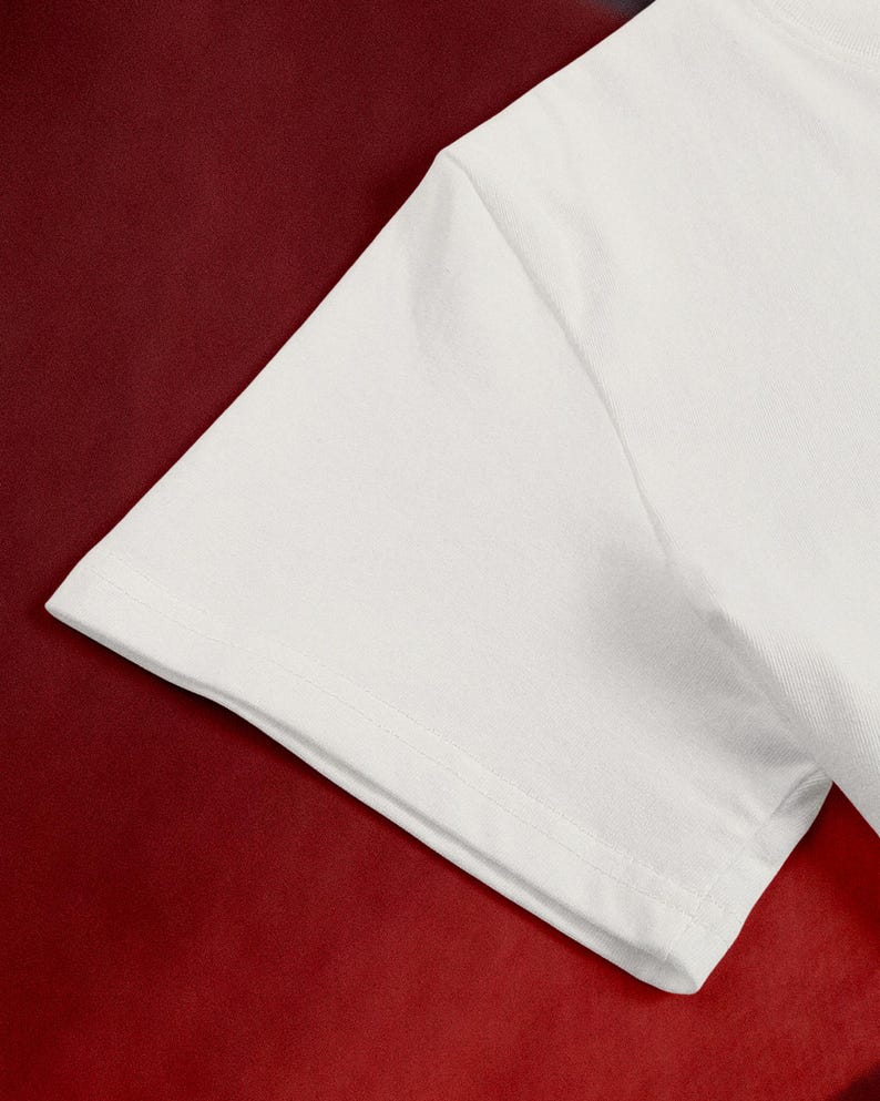 May include: Close-up of a white t-shirt sleeve against a deep red background. The sleeve is made of a smooth, opaque fabric, with visible stitching along the hem and seams. The contrast between the white fabric and the red backdrop creates a striking visual.