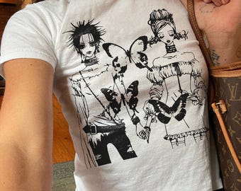 May include: White t-shirt featuring a black and white graphic of two anime-style figures and butterflies. The figures are dressed in detailed outfits. The shirt is paired with blue jeans.